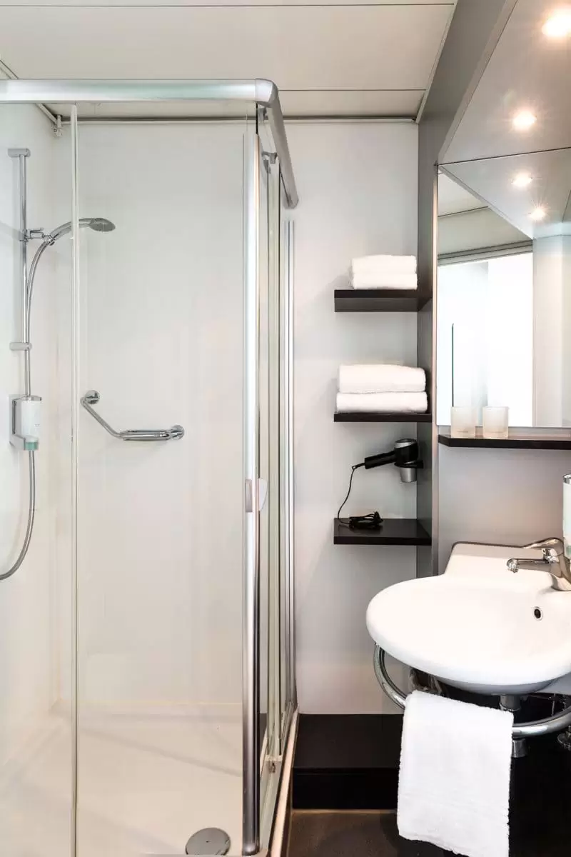 Kleines Badezimmer mit Dusche, Waschbecken und einem Spiegel sowie Handtüchern und einem Haartrockner.