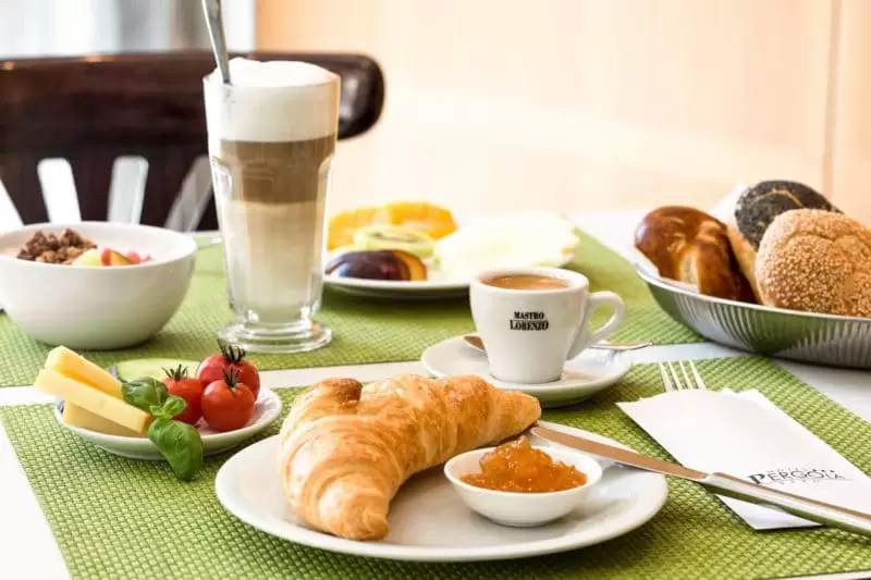 Gedeckter Frühstückstisch mit Backwaren, Gemüse, Käse und zwei Kaffees.
