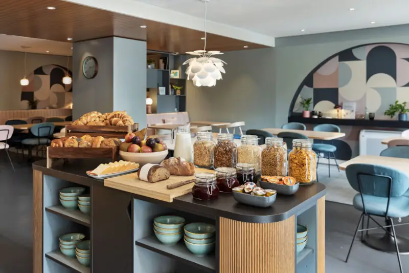 Buffetstation im Frühstücksraum mit Backwaren, Cerealien und Milch.