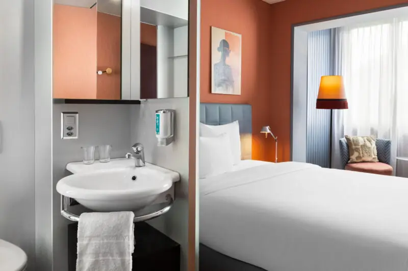 Interior of a business bedroom at Hotel La Pergola, showcasing a bed, sink, and toilet in a compact layout.  