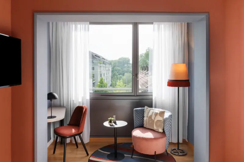 Interior of a comfort room twin at Hotel La Pergola with vibrant orange walls and a chair.  