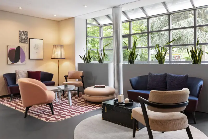 Moderner Loungebereich in der Hotellobby mit Sesseln, Sofas, Couchtisch und großen Fenster mit Blick ins Grüne.