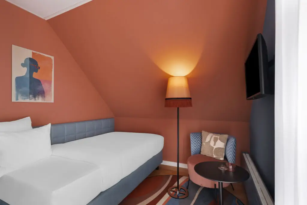 A welcoming single room at Hotel La Pergola with a bed, chair, and lamp, perfect for relaxation.