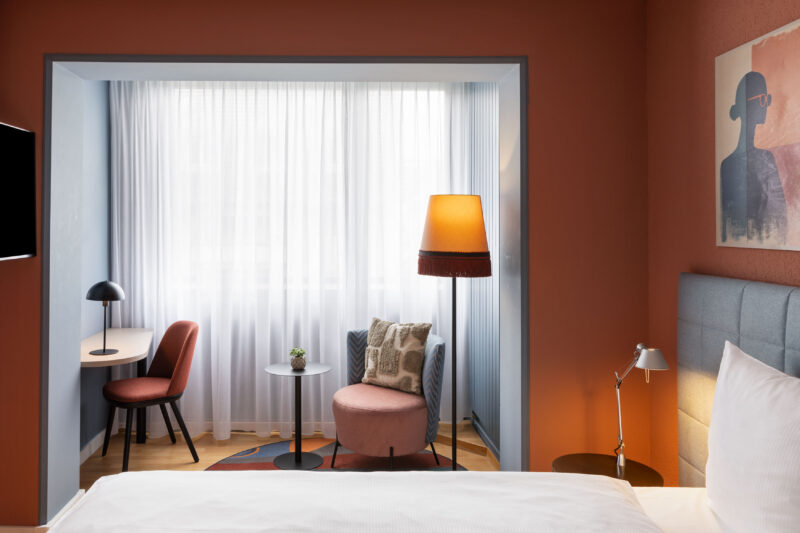 Modernes Hotelzimmer im Hotel La Pergola mit Bett, orangefarbenen Wänden und gemütlicher Sitzecke am Fenster.
